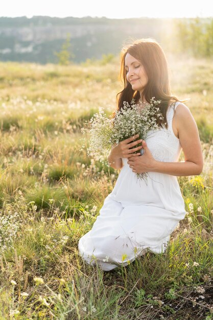 Vista frontale della donna che posa nell'erba con i fiori
