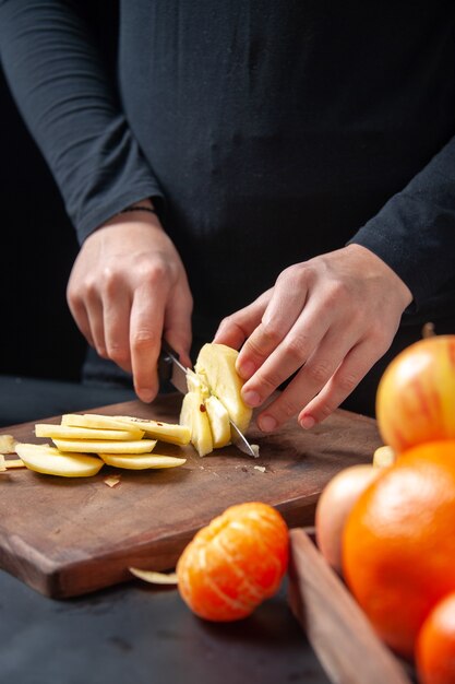 Vista frontale della donna che taglia a pezzi la frutta fresca della mela in vassoio di legno sul tavolo da cucina