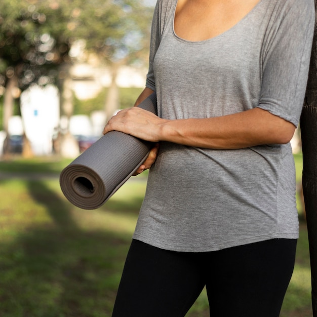 Vista frontale della donna che tiene materassino yoga all'aperto