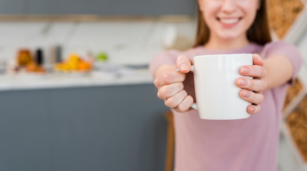 Vista frontale della donna che tiene tazza con cucina sfocato