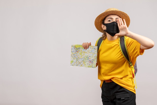 Vista frontale della donna che viaggia con maschera nera che tiene mappa chiamando qualcuno sul muro bianco