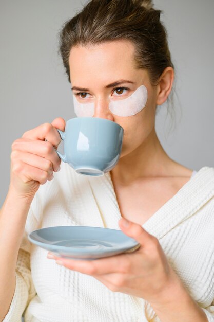 Vista frontale della donna con le bende sull'occhio che beve caffè