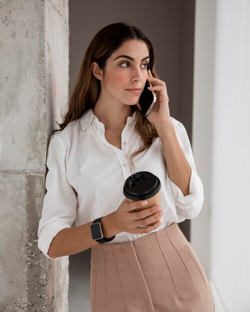 Vista frontale della donna di affari che parla al telefono mentre beve il caffè