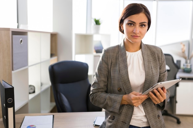 Vista frontale della donna di affari che propone con la compressa in ufficio