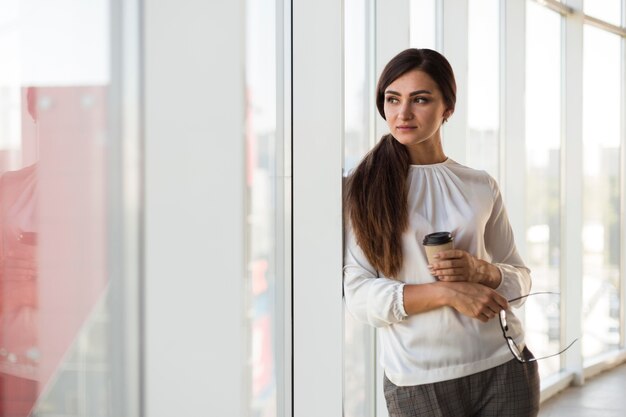 Vista frontale della donna di affari che propone con la tazza di caffè