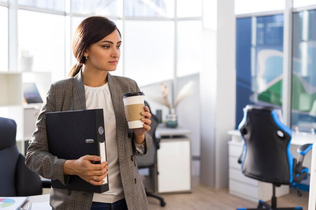 Vista frontale della donna di affari che tiene caffè e legante