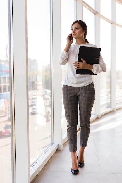 Vista frontale della donna di affari che tiene legante e parlando al telefono