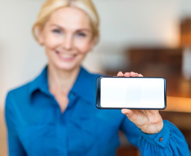 Vista frontale della donna di affari di smiley defocused che tiene smartphone