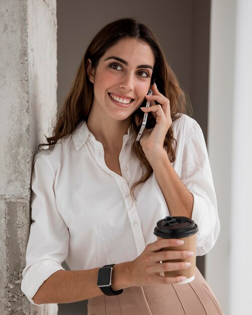 Vista frontale della donna di affari di smiley parlando al telefono mentre beve il caffè