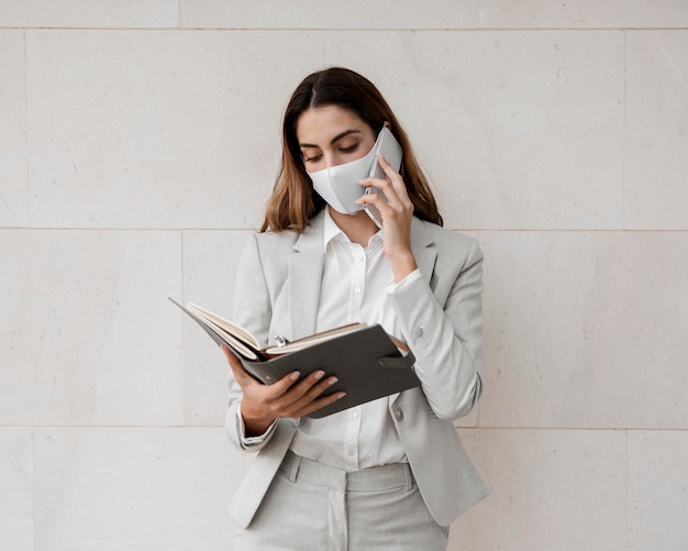 Vista frontale della donna di affari elegante con la maschera che parla sul telefono