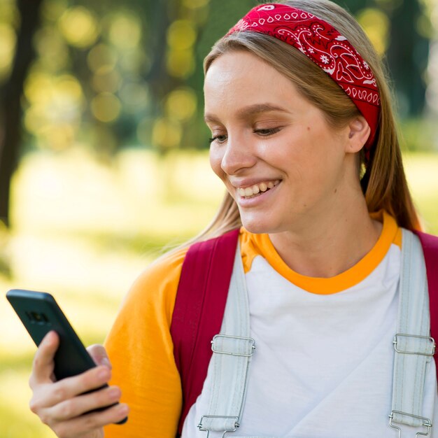 Vista frontale della donna di smiley che esamina smartphone all'aperto