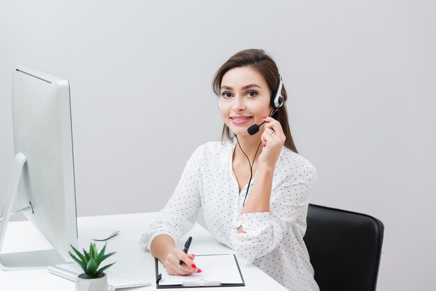 Vista frontale della donna di smiley che propone con la cuffia avricolare allo scrittorio