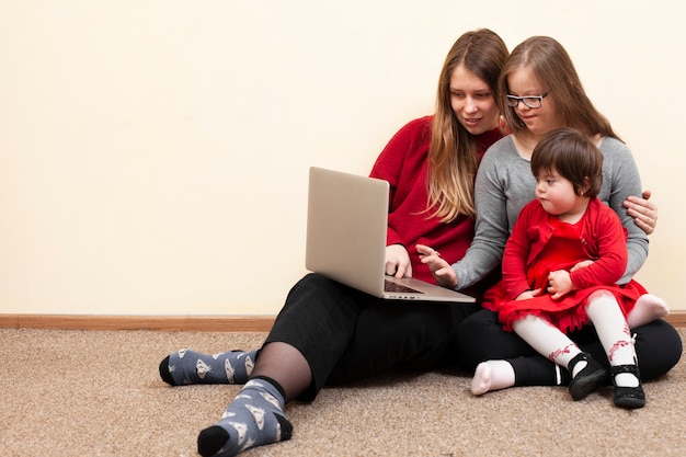 Vista frontale della donna e dei bambini con sindrome di down che esaminano computer portatile
