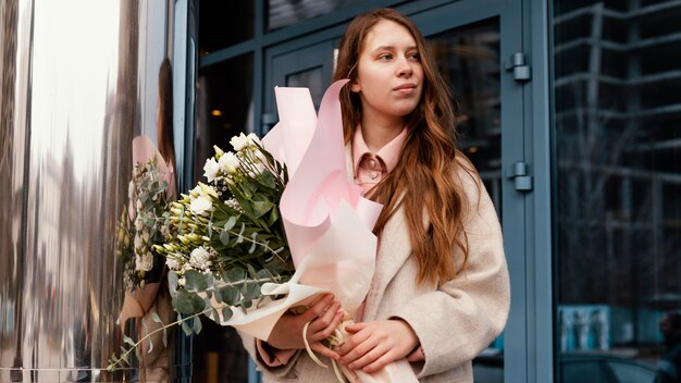 Vista frontale della donna elegante che tiene un mazzo di fiori all'aperto