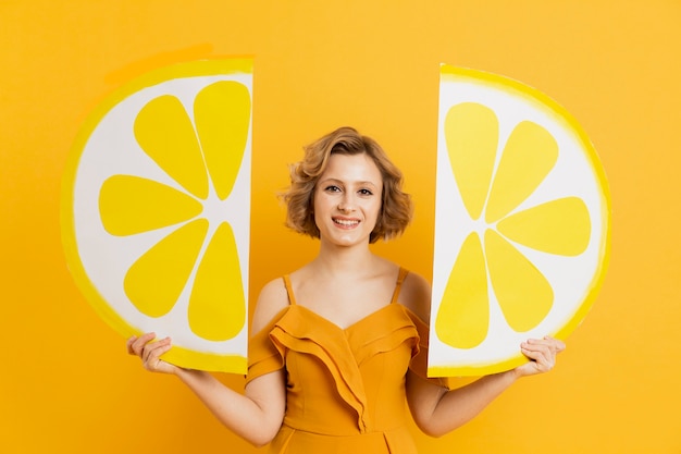 Vista frontale della donna felice che posa con le decorazioni delle fette del limone