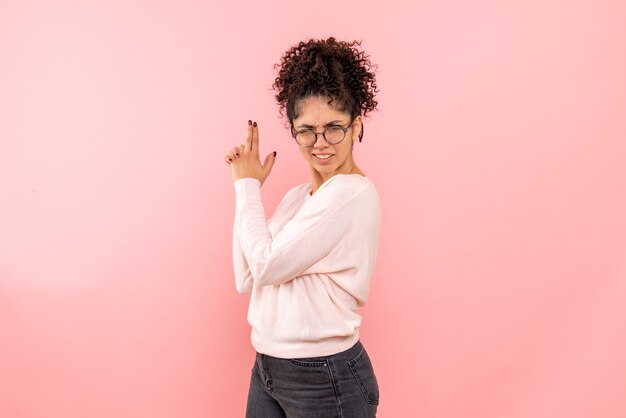 Vista frontale della donna graziosa che imita la pistola che tiene sul rosa