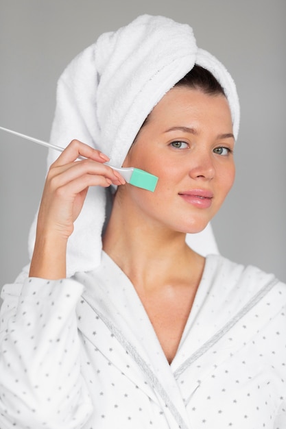 Vista frontale della donna in accappatoio e asciugamano che applica la cura della pelle