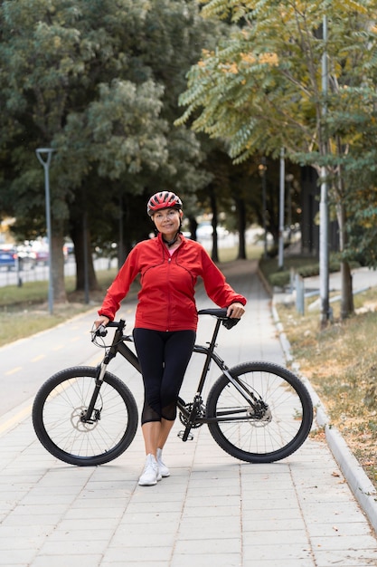 Vista frontale della donna maggiore che propone all'aperto con la bici