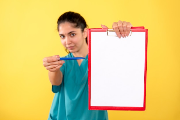 Vista frontale della donna medico in uniforme che punta alla carta sulla parete gialla