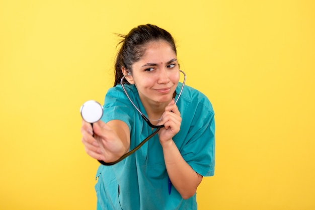 Vista frontale della donna medico in uniforme utilizzando il suo stetoscopio sulla parete gialla