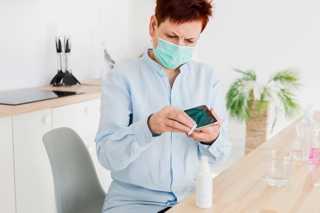 Vista frontale della donna più anziana che disinfetta il suo smartphone