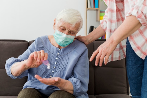 Vista frontale della donna più anziana che usando disinfettante per le mani mentre indossando maschera medica