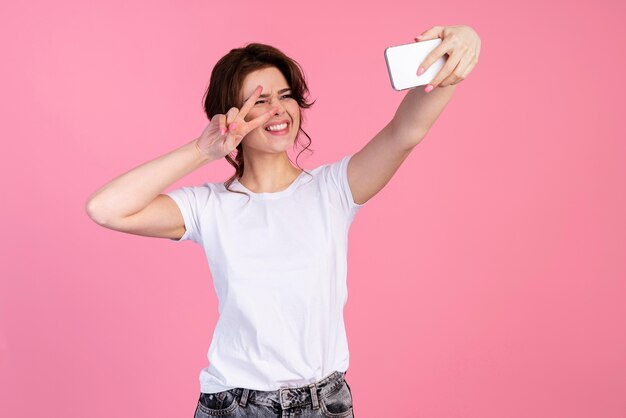 Vista frontale della donna sorridente prendendo un selfie e facendo segno di pace