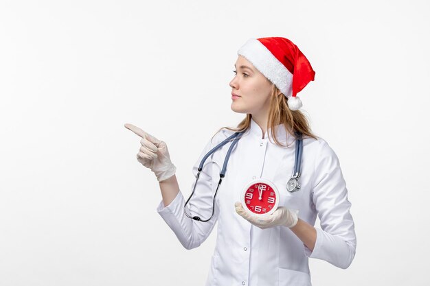 Vista frontale della dottoressa che tiene l'orologio sul muro bianco