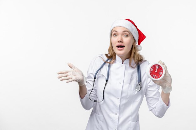 Vista frontale della dottoressa che tiene l'orologio sul muro bianco