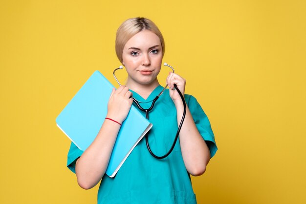 Vista frontale della dottoressa con analisi e stetoscopio sulla parete gialla