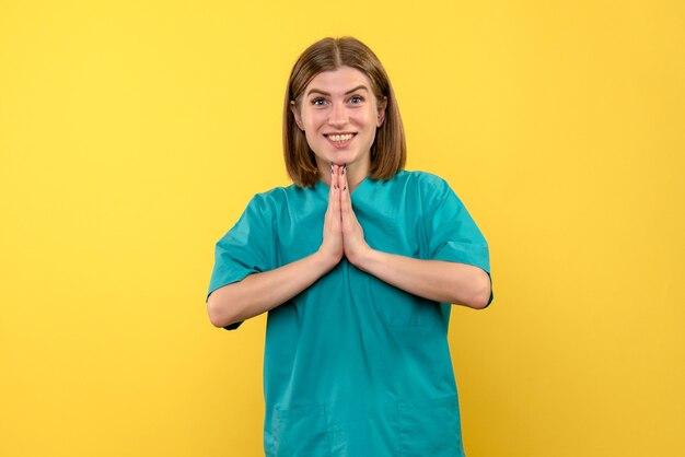 Vista frontale della dottoressa con espressione di preghiera sulla parete gialla