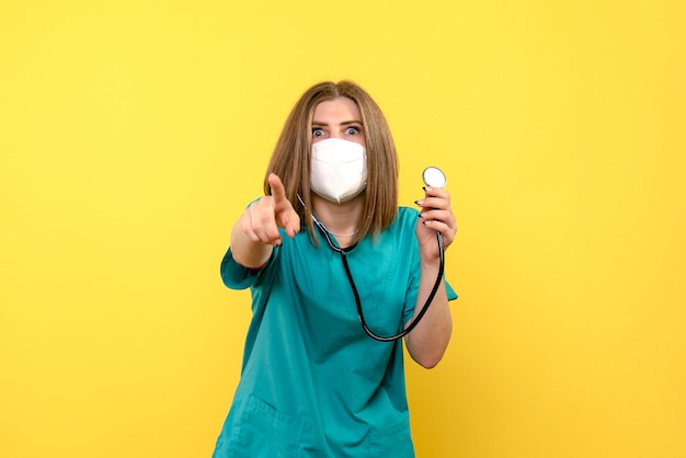 Vista frontale della dottoressa con maschera e tonometro sulla parete gialla