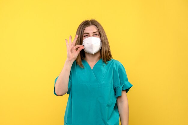 Vista frontale della dottoressa con maschera protettiva sulla parete gialla