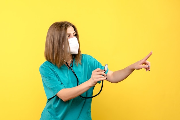 Vista frontale della dottoressa con maschera sterile sulla parete gialla