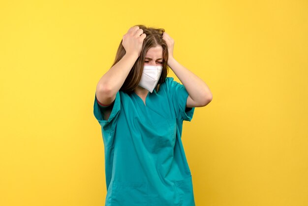 Vista frontale della dottoressa con maschera sulla parete gialla