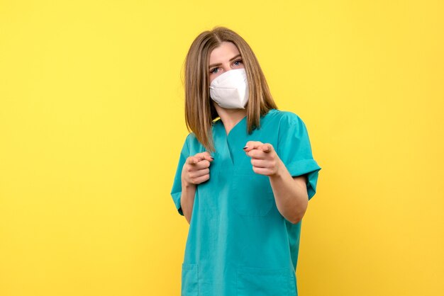 Vista frontale della dottoressa con maschera sulla parete gialla