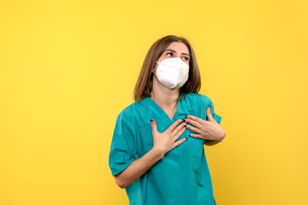 Vista frontale della dottoressa con maschera sulla parete gialla