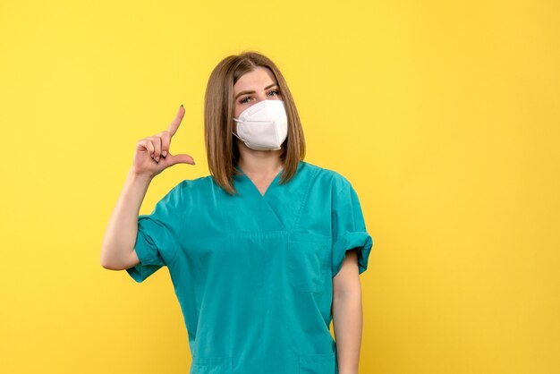 Vista frontale della dottoressa con maschera sulla parete gialla