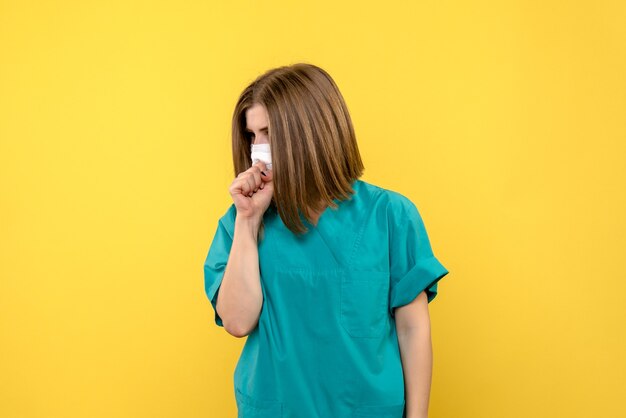 Vista frontale della dottoressa con maschera sulla parete gialla