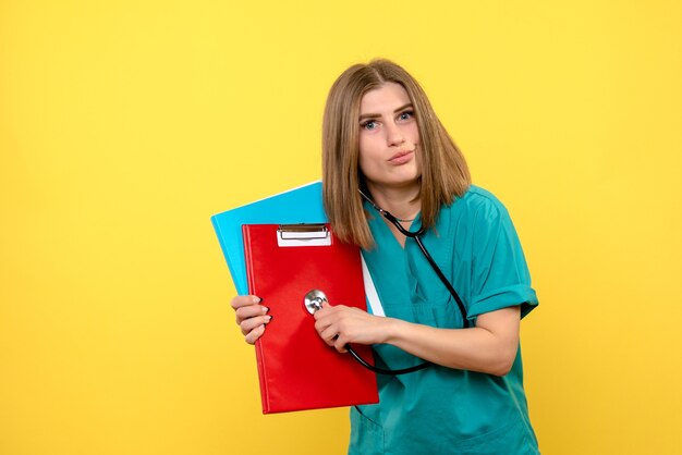 Vista frontale della dottoressa con tonometro e file sulla parete gialla