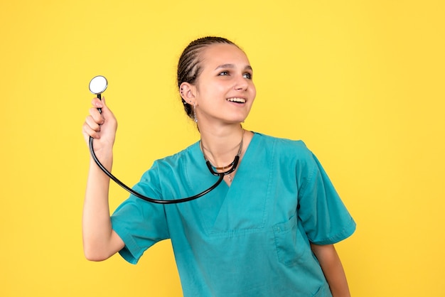 Vista frontale della dottoressa in camicia medica con lo stetoscopio sulla parete gialla