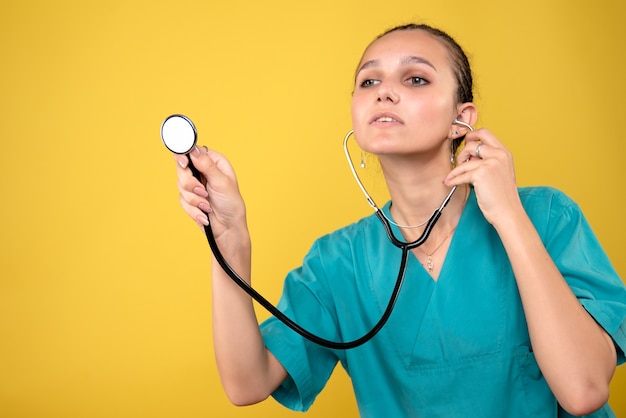 Vista frontale della dottoressa in camicia medica con lo stetoscopio sulla parete gialla