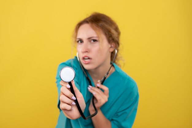 Vista frontale della dottoressa in camicia medica con lo stetoscopio sulla parete gialla