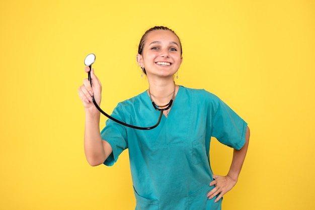 Vista frontale della dottoressa in camicia medica con lo stetoscopio sulla parete gialla