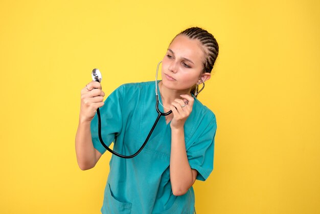 Vista frontale della dottoressa in camicia medica con lo stetoscopio sulla parete gialla