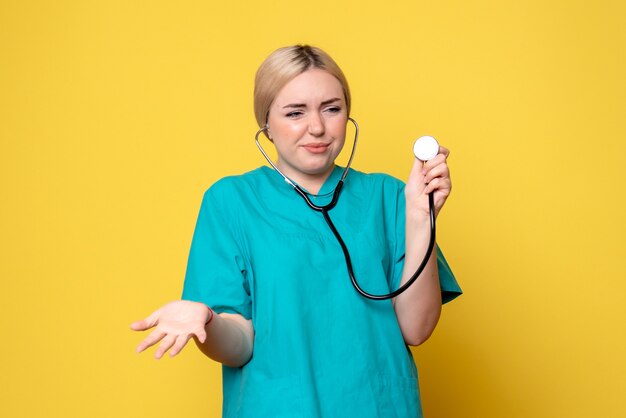 Vista frontale della dottoressa in camicia medica con lo stetoscopio sulla parete gialla