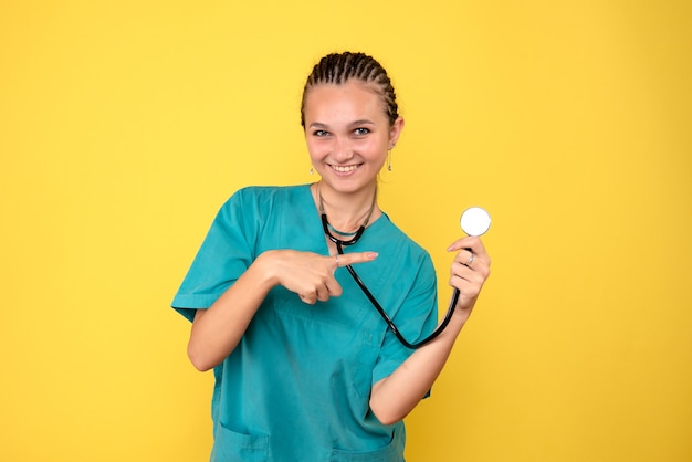 Vista frontale della dottoressa in camicia medica con lo stetoscopio sulla parete gialla