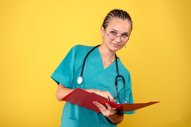 Vista frontale della dottoressa in camicia medica scrivere note sulla parete gialla