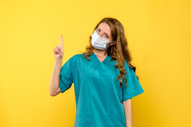 Vista frontale della dottoressa in maschera sulla parete gialla