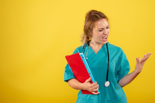 Vista frontale della dottoressa in tuta medica che tiene analisi diverse sulla parete gialla